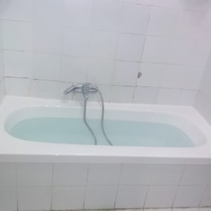 אמבטיה עם מים וברז מתכת על קיר מרוצף