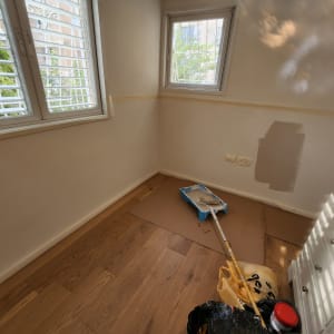 חדר עם קיר צבוע חלקית, מגש צבע ומברשת על הרצפה