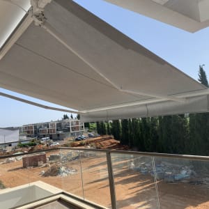 סוכך אפור פתוח על מרפסת עם מעקה זכוכית.