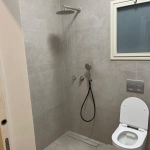 חדר רחצה משופץ עם מקלחון, חיפוי אריחים אפור ואסלה תלויה