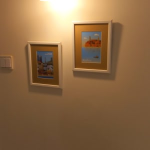 קיר פנים צבוע בגוון בהיר ועליו מנורת קיר ותמונות ממוסגרות