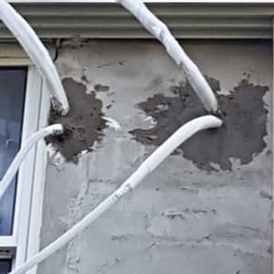 צינורות לבנים מחוברים לקיר בטון עם טיח