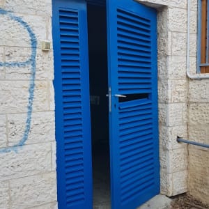 דלתות תריס כחולות פתוחות בקיר אבן