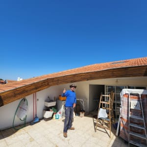 גג רעפים עם אדם עומד ליד סולם וחפצים