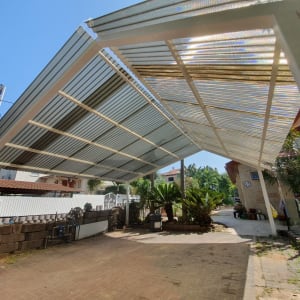 גג מתכת מעל שביל עם צמחים ירוקים בצדדים