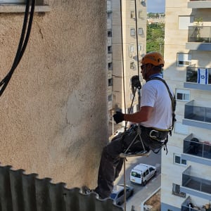 אדם עם קסדה ורתמה עובד בגובה על קיר בניין