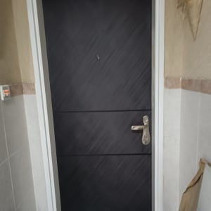 דלת שחורה עם ידית מתכת כסופה במסגרת לבנה