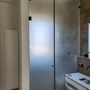 דלת זכוכית חלבית עם ידיות שחורות בחדר אמבטיה