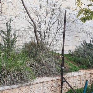 גדר מתכת דקה עם עמודים תומכים ליד קיר אבן