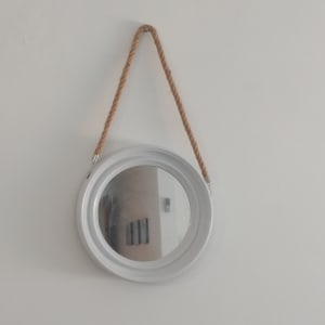 מראה עגולה תלויה על חבל על קיר לבן