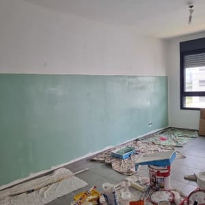 קיר צבוע בחצי ירוק, כלים וחומרי צביעה על הרצפה