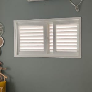 מזגן מותקן על קיר מעל חלון עם תריסים