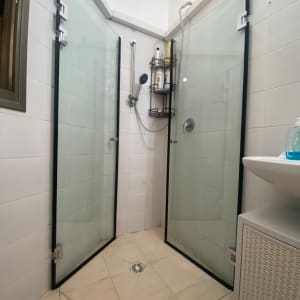 מקלחון עם דלתות זכוכית ומדף עם מוצרי רחצה