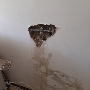 צינור מתכת חשוף בקיר עם נזקי רטיבות