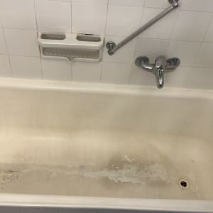 אמבטיה לבנה עם כתמים, ברז ומחזיק סבון על קיר אריחים לבנים.