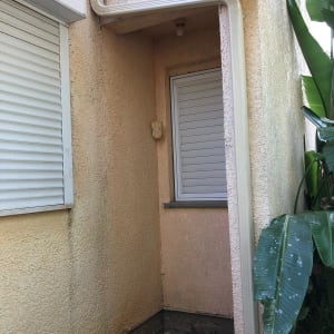 מרזב לבן מחובר לגג בית עם קיר טיח