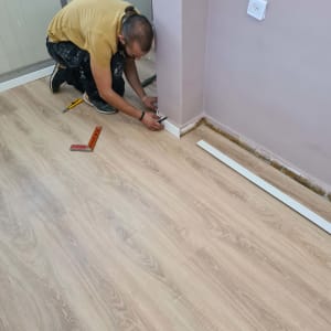 אדם מתקין פרקט עץ עם כלי עבודה על הרצפה