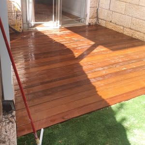 מרפסת עץ רטובה עם מטאטא ומגב על דשא סינתטי