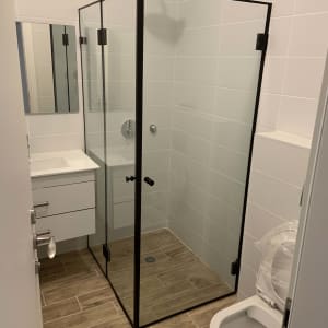 מקלחון זכוכית עם דלתות שחורות ורצפת עץ