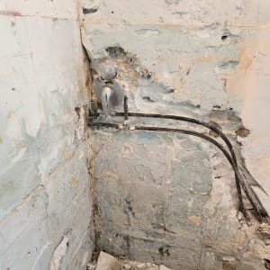 קיר מתקלף עם צינורות חשופים ושברי טיח על הרצפה