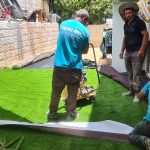 עובדים מתקינים דשא סינתטי בחצר קטנה