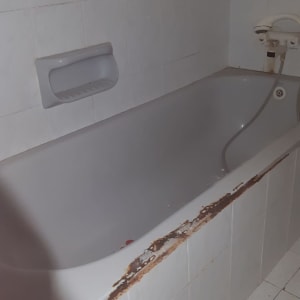 אמבטיה עם חיפוי פגום וקיר אריחים לבן