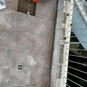 אדם עם כפפות כתומות משתמש במקדחה על רצפה מרוצפת