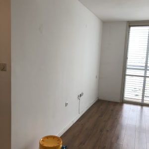 דלי צבע צהוב על רצפת עץ ליד קיר לבן