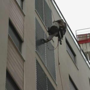 אדם תלוי על חבל ליד תריסים בבניין גבוה