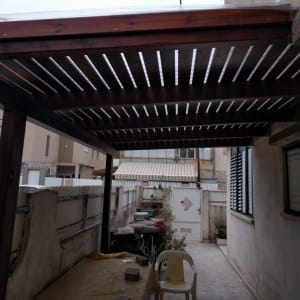 פרגולה מעץ בחצר עם שולחן וכיסא פלסטיק