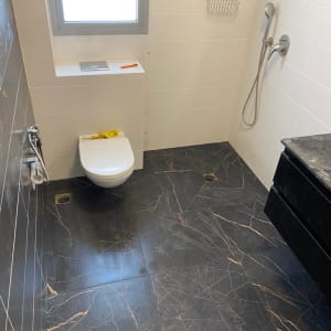 חדר אמבטיה עם רצפת שיש כהה, מקלחת ושירותים מותקנים.