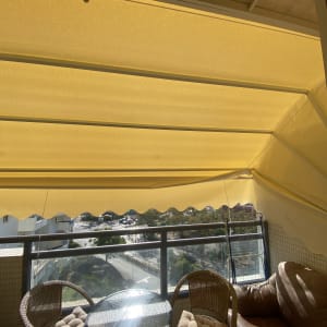 סוכך צהוב תלוי מעל מרפסת עם שולחן וכיסאות