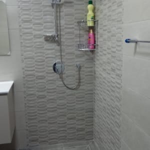 מקלחת משופצת עם אריחים אפורים ומדף מתכת