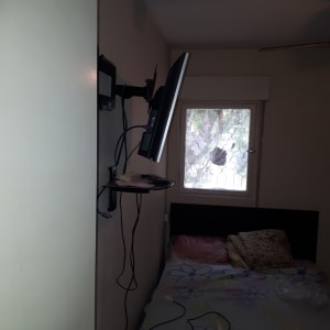 חדר עם מיטה, מסך תלוי על הקיר, חלון עם סורגים