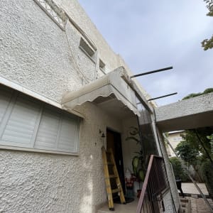 סוכך לבן מותקן מעל כניסה לבית עם תומכות מתכת.
