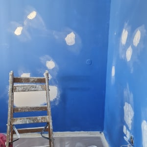 קיר כחול עם תיקוני צבע, סולם ודלי צבע