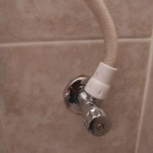 ברז מתכת עם צינור מחובר על קיר קרמיקה