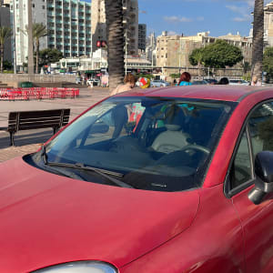 מכונית אדומה חונה ליד מדרכה עם עצי דקל ברקע