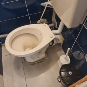 אסלה עם חיבורי צנרת גלויים ותיקונים סביב הבסיס