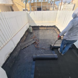 אדם מיישם יריעות איטום על גג בעזרת מבער גז