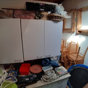 ארון לבן עם ידיות, כיסאות עץ נערמים, קופסאות וציוד מאוחסנים