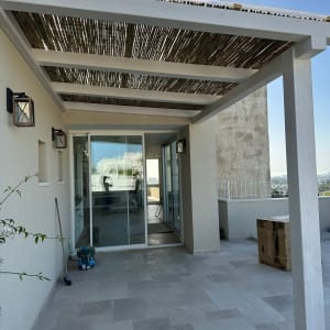 פרגולה מעץ עם גג קנים מעל מרפסת מרוצפת