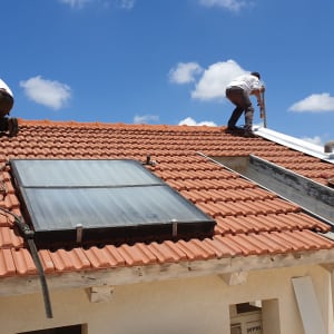 שני אנשים עובדים על גג רעפים עם קולטי שמש