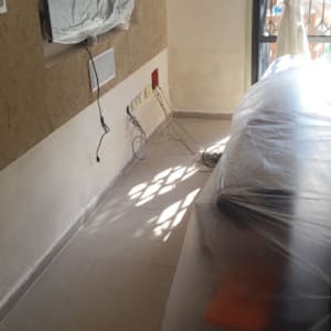 חדר עם קיר צבוע חלקית וציוד מכוסה בניילון