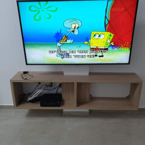 טלוויזיה תלויה על קיר מעל מדף עץ עם כבלים