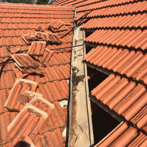 רעפים כתומים שבורים על גג עם תעלה מתכתית