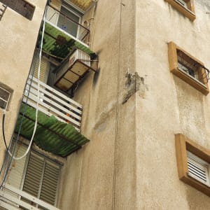 מרפסת עם גגון ירוק ומזגן ישן על קיר בניין