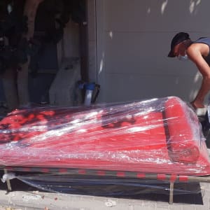 אדם עוטף ספה אדומה בניילון לקראת מעבר