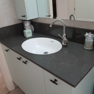 משטח שיש כהה עם כיור עגול וברז מתכת