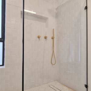 מקלחון זכוכית עם אריחים לבנים וברזים מוזהבים